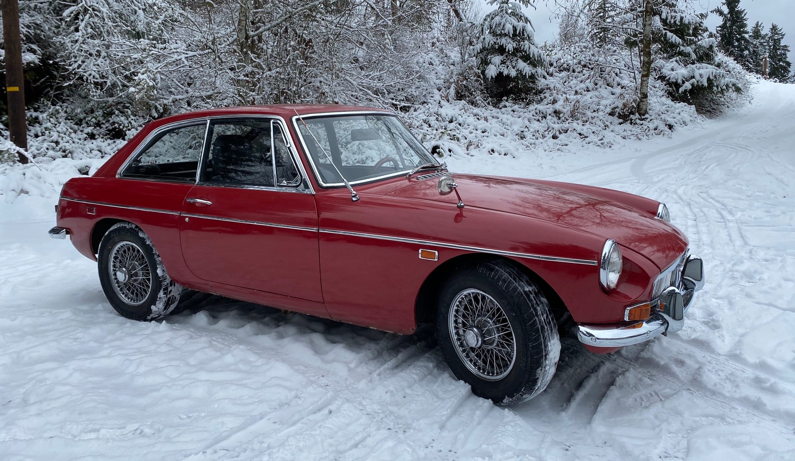 A red 1969 MGB GT parked in a snowy driveway.