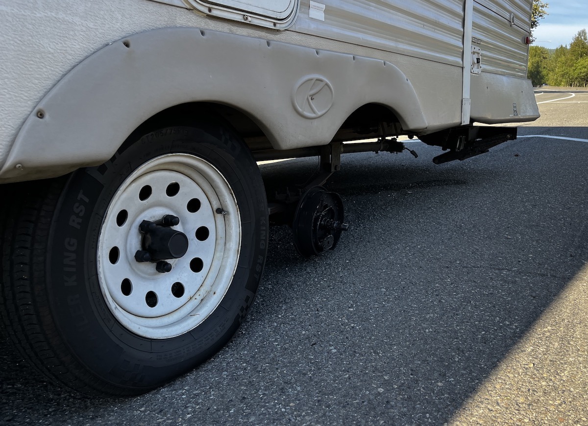 A tandem axle RV trailer with a missing wheel and tire.