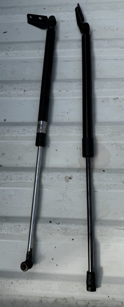 Old worn Subaru Outback liftgate struts next to new replacement struts